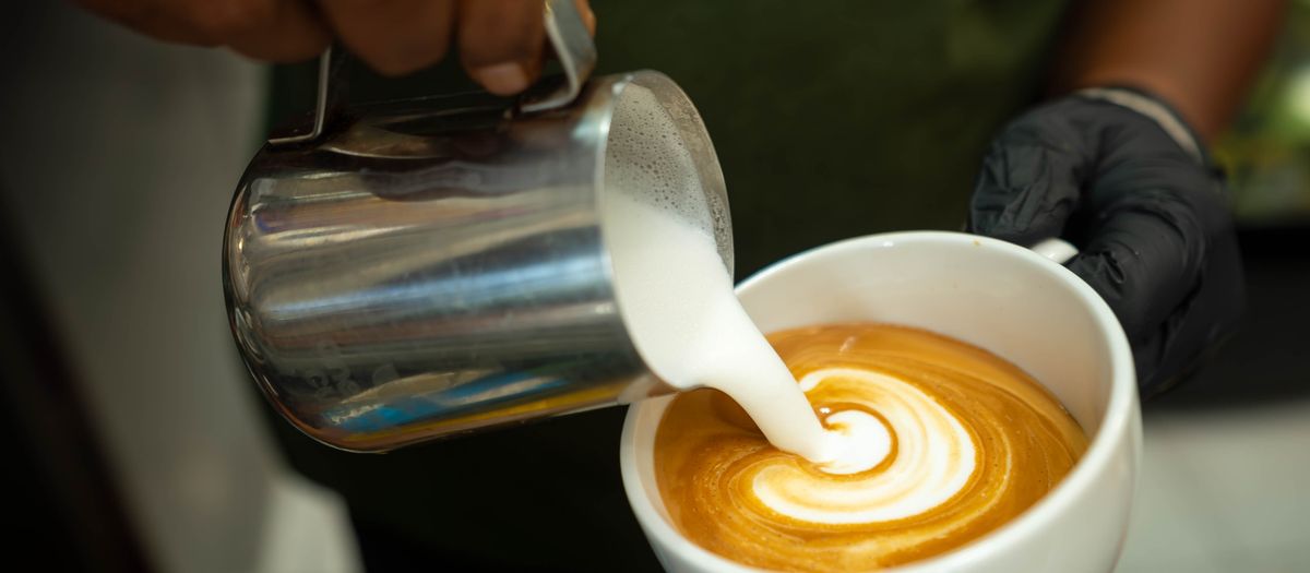Close-up of barista pouring milk to create intricate latte art in a steaming cup of coffee.