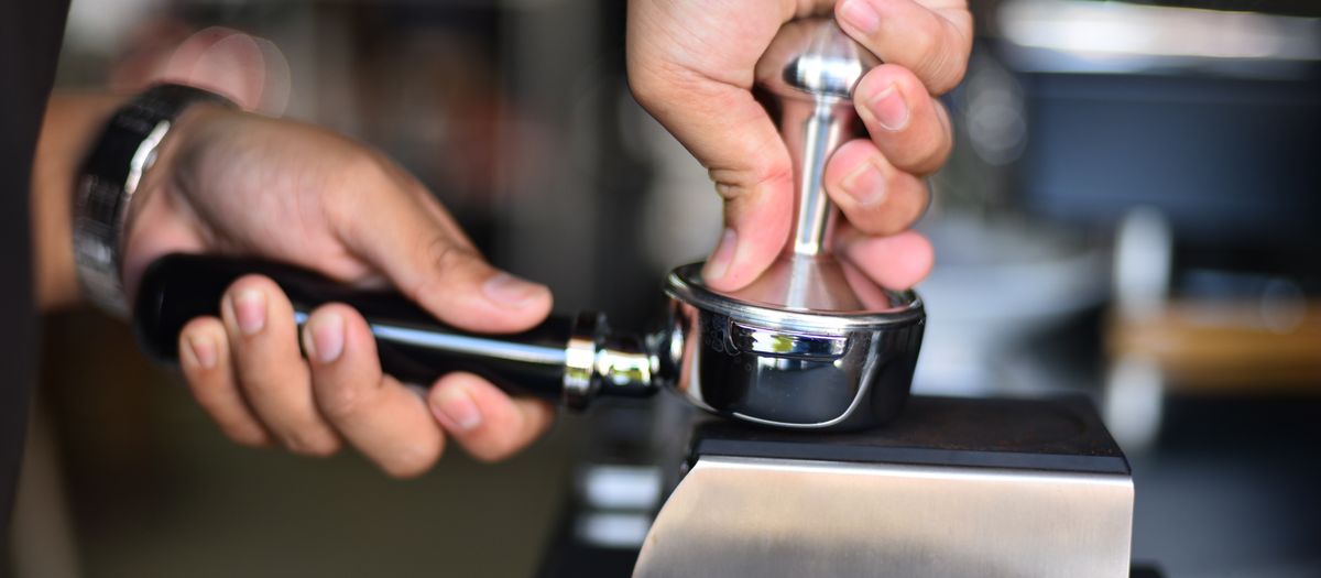 Close-up of a barista's hands using a tamper to prepare espresso in a portafilter.