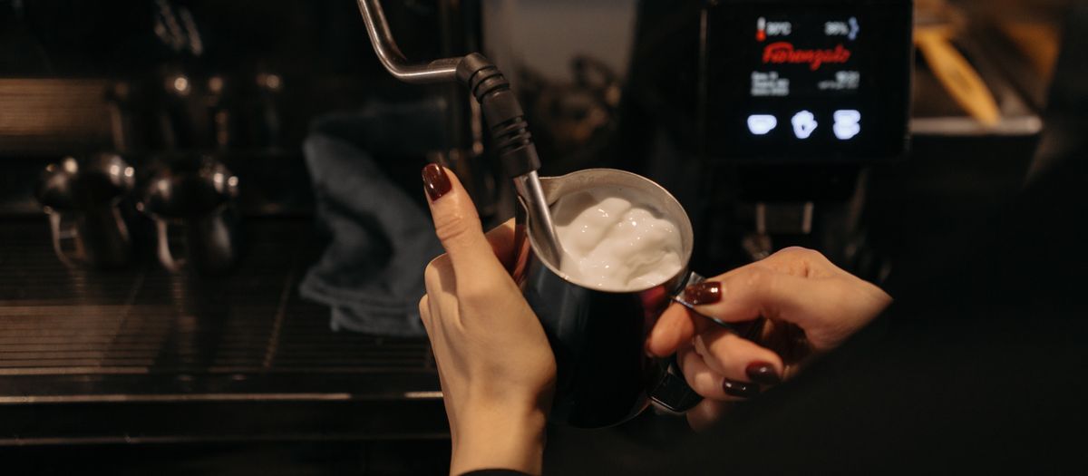A barista uses a steam wand to froth milk in a café, focusing on coffee preparation.